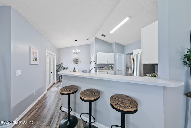 13254 Karla Cove Ln, Jacksonville, FL 32225 - kitchen with stainless steel refrigerator with ice dispenser, white cabinets, wood finished floors, vaulted ceiling, and a kitchen bar