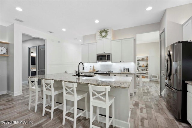 395 Jennie Lake Ct, Saint Johns, FL 32095 - kitchen with appliances with stainless steel finishes, light wood-style flooring, a breakfast bar area, light stone counters, and recessed lighting