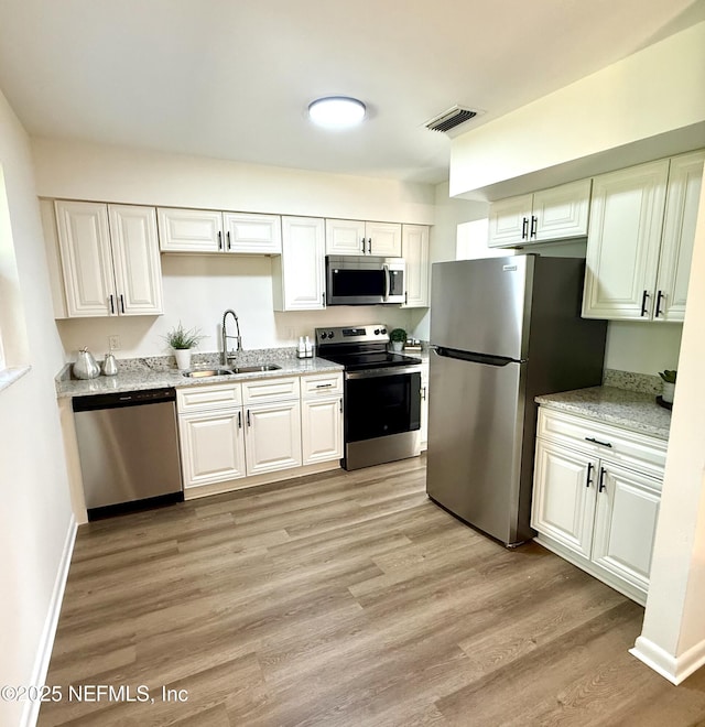 2536 Wedgefield Blvd, Jacksonville, FL 32211 - kitchen with stainless steel appliances, light wood-style flooring, white cabinets, and light stone counters