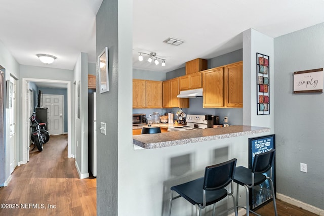 113 Oceangate Dr, Atlantic Beach, FL 32233 - kitchen with under cabinet range hood, white electric stove, light wood-type flooring, a breakfast bar, and a peninsula