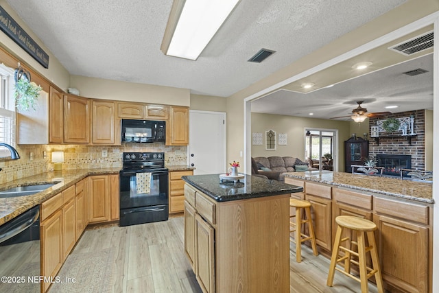 4115 Wilcrest Cir W, Jacksonville, FL 32277 - kitchen featuring black appliances, a textured ceiling, a breakfast bar area, open floor plan, and light wood-style floors