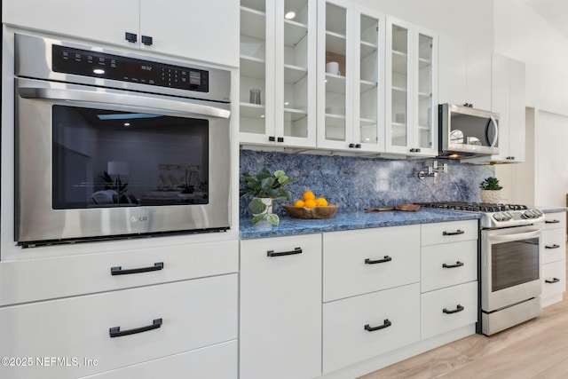 1465 Lambert Ave, Flagler Beach, FL 32136 - kitchen with stainless steel appliances, glass insert cabinets, backsplash, light wood-style flooring, and white cabinetry