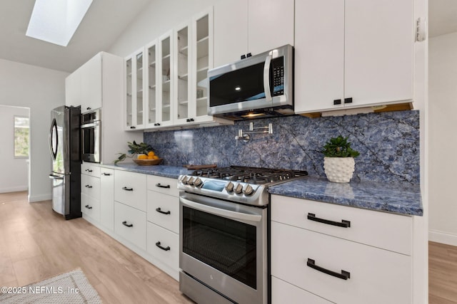 1465 Lambert Ave, Flagler Beach, FL 32136 - kitchen featuring appliances with stainless steel finishes, tasteful backsplash, a skylight, light wood-type flooring, and glass insert cabinets