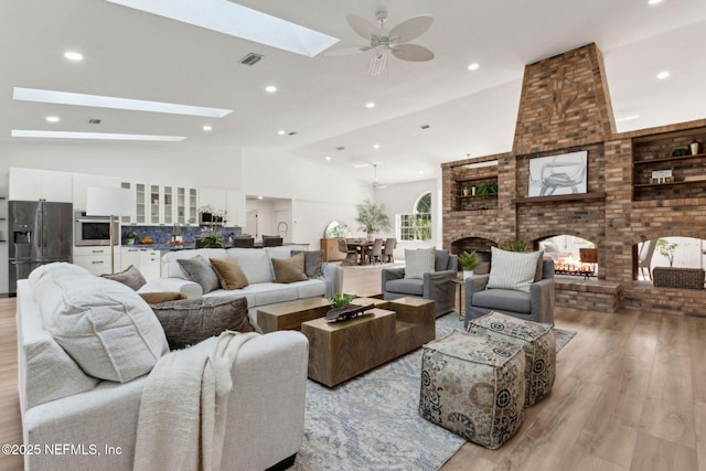 1465 Lambert Ave, Flagler Beach, FL 32136 - living room featuring a skylight, a brick fireplace, light wood-style flooring, vaulted ceiling, and a ceiling fan