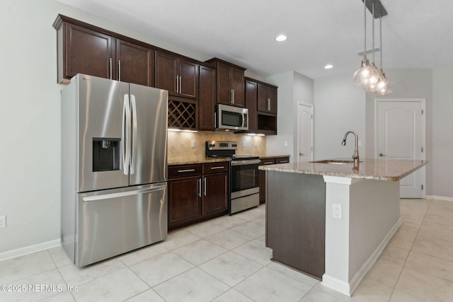 94032 Woodbrier Cir, Fernandina Beach, FL 32034 - kitchen featuring appliances with stainless steel finishes, backsplash, light stone countertops, a center island with sink, and dark brown cabinets