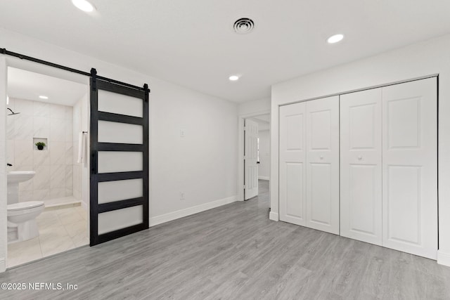 6285 Spring Forest Cir, Jacksonville, FL 32216 - unfurnished bedroom featuring a barn door, ensuite bath, a closet, recessed lighting, and wood finished floors