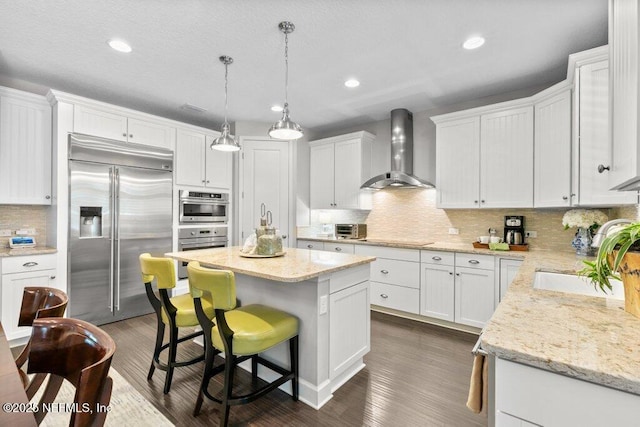 26 Traveler Palm Ct, Ponte Vedra Beach, FL 32082 - kitchen featuring appliances with stainless steel finishes, wall chimney range hood, a center island, white cabinetry, and decorative backsplash