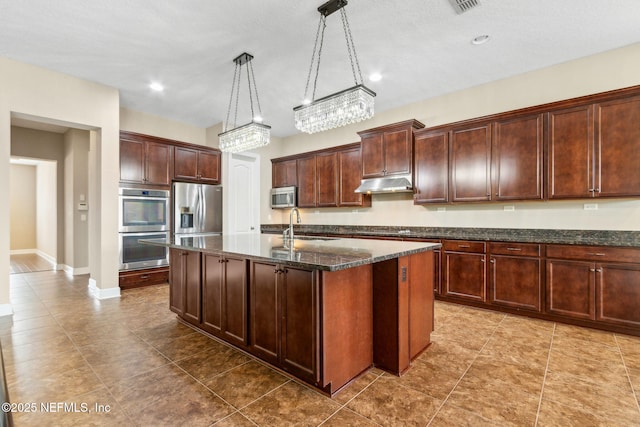 1306 Warbler Way, Middleburg, FL 32068 - kitchen with appliances with stainless steel finishes, under cabinet range hood, dark stone countertops, a kitchen island with sink, and pendant lighting