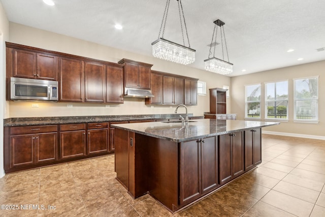 1306 Warbler Way, Middleburg, FL 32068 - kitchen with stainless steel microwave, under cabinet range hood, recessed lighting, a center island with sink, and dark stone counters