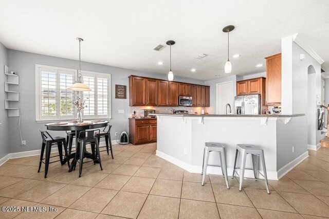 11598 Wynnfield Lakes Cir, Jacksonville, FL 32246 - kitchen featuring appliances with stainless steel finishes, a breakfast bar area, a peninsula, light tile patterned floors, and decorative light fixtures
