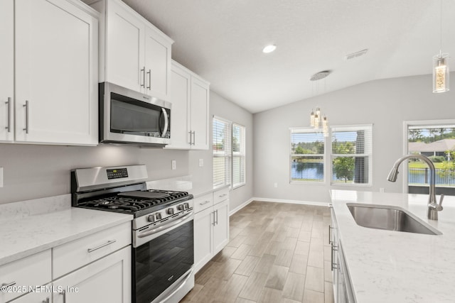 83687 Nether St, Fernandina Beach, FL 32034 - kitchen featuring appliances with stainless steel finishes, vaulted ceiling, white cabinets, light wood-style flooring, and decorative light fixtures