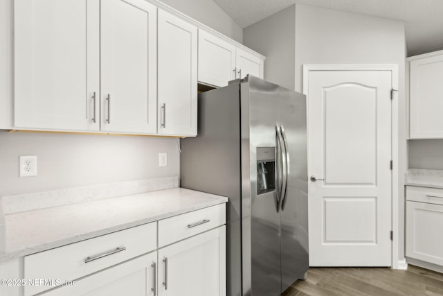 83687 Nether St, Fernandina Beach, FL 32034 - kitchen with stainless steel fridge, white cabinetry, light wood-style floors, and light stone counters