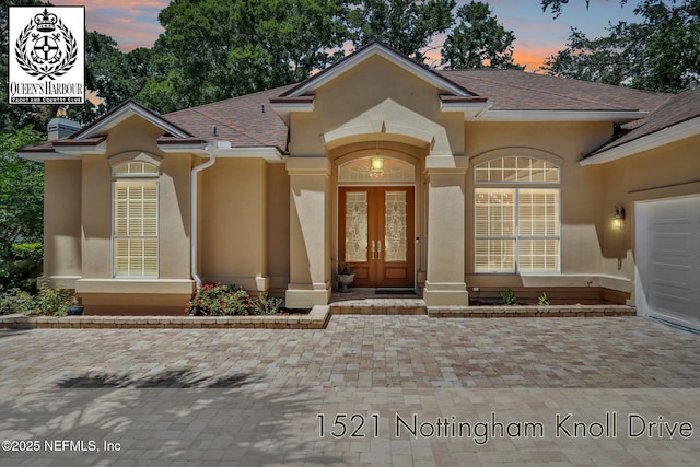 1521 Nottingham Knoll Dr, Jacksonville, FL 32225 - exterior entry at dusk featuring stucco siding, a shingled roof, french doors, and an attached garage