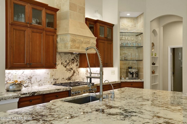 1521 Nottingham Knoll Dr, Jacksonville, FL 32225 - kitchen featuring custom exhaust hood, light stone counters, backsplash, arched walkways, and brown cabinetry