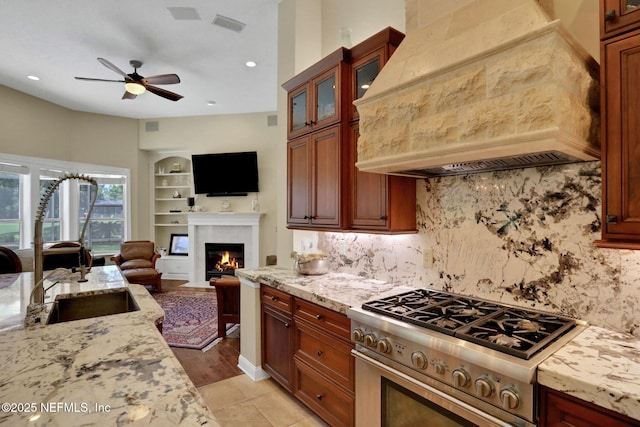 1521 Nottingham Knoll Dr, Jacksonville, FL 32225 - kitchen with custom exhaust hood, high end stainless steel range, open floor plan, ceiling fan, and a fireplace with flush hearth