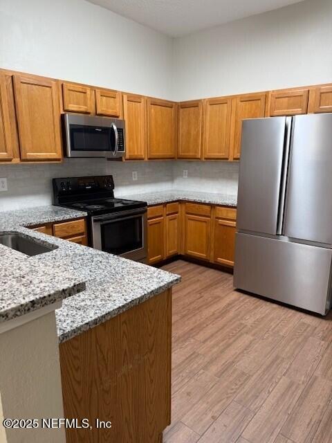 9556 Armelle Way Unit 2, Jacksonville, FL 32257 - kitchen with stainless steel appliances, light stone counters, brown cabinets, light wood finished floors, and backsplash
