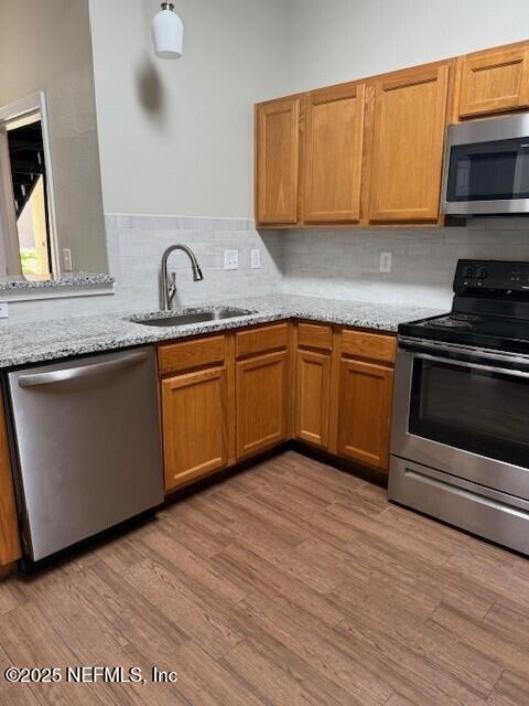 9556 Armelle Way Unit 2, Jacksonville, FL 32257 - kitchen featuring stainless steel appliances, tasteful backsplash, light wood-style floors, light stone counters, and brown cabinetry