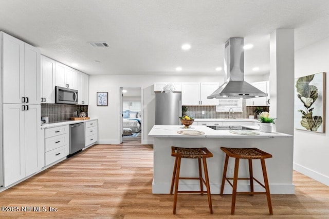 2571 Montreal St, Jacksonville, FL 32233 - kitchen featuring island range hood, stainless steel appliances, light wood-style flooring, decorative backsplash, and a kitchen breakfast bar