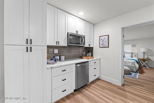 2571 Montreal St, Jacksonville, FL 32233 - kitchen featuring stainless steel appliances, backsplash, white cabinets, light wood finished floors, and a textured ceiling