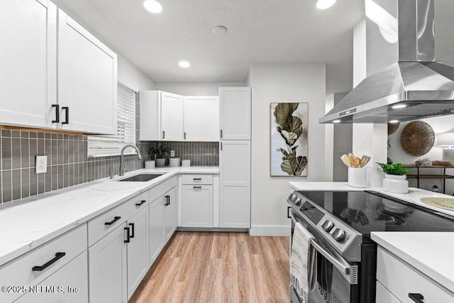 2571 Montreal St, Jacksonville, FL 32233 - kitchen with stainless steel electric range oven, wall chimney exhaust hood, light wood finished floors, white cabinets, and tasteful backsplash