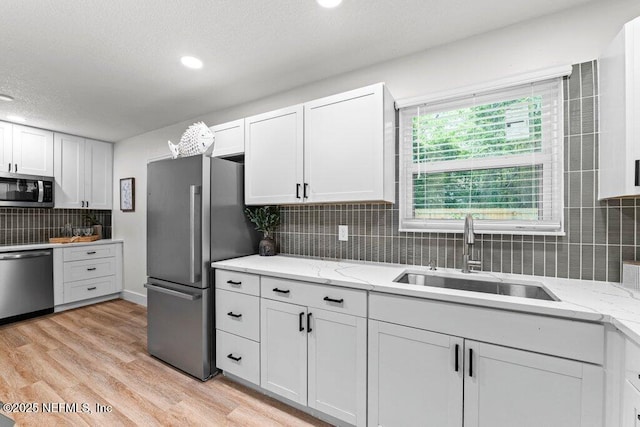 2571 Montreal St, Jacksonville, FL 32233 - kitchen with stainless steel appliances, backsplash, light wood-type flooring, white cabinetry, and a textured ceiling