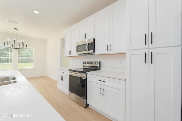 1861 Openwoods Rd, Middleburg, FL 32068 - kitchen with appliances with stainless steel finishes, light wood-style floors, light countertops, white cabinetry, and a chandelier