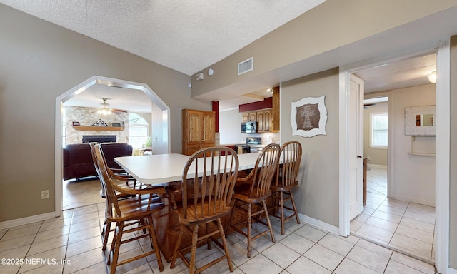 5110 Janice Cir E, Jacksonville, FL 32210 - dining space featuring light tile patterned floors, a fireplace, arched walkways, a textured ceiling, and ceiling fan