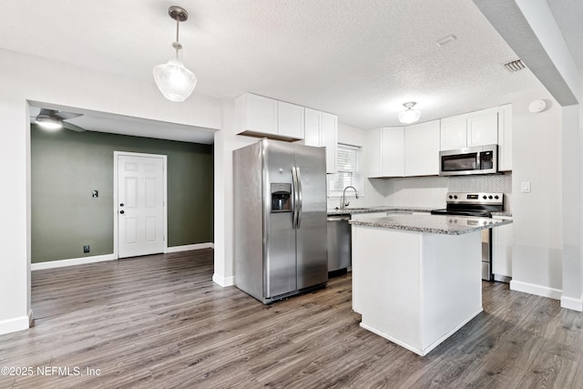 3349 Gilmore St, Jacksonville, FL 32205 - kitchen featuring appliances with stainless steel finishes, dark wood-style floors, a center island, white cabinets, and a textured ceiling