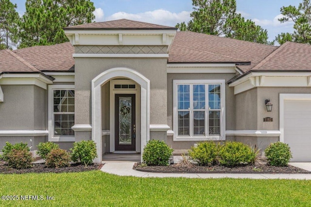 1103 Orchard Oriole Pl, Middleburg, FL 32068 - doorway to property featuring a shingled roof, an attached garage, stucco siding, and a lawn