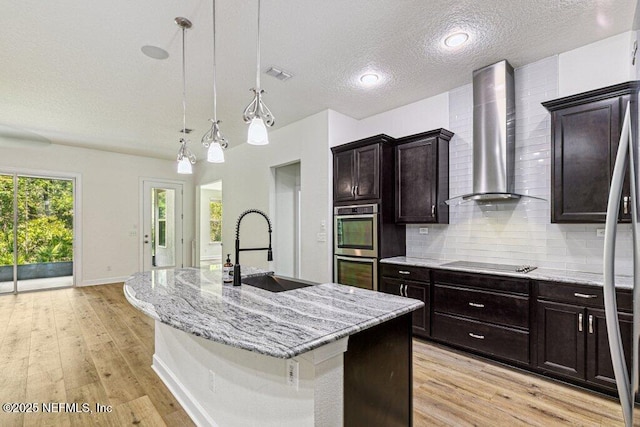 1103 Orchard Oriole Pl, Middleburg, FL 32068 - kitchen featuring wall chimney exhaust hood, light stone counters, light wood finished floors, backsplash, and a textured ceiling