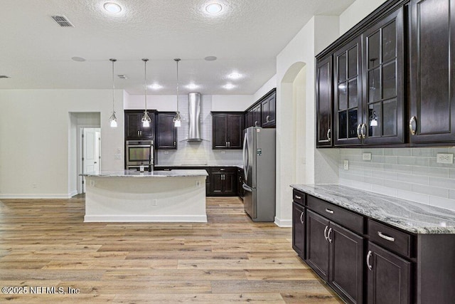1103 Orchard Oriole Pl, Middleburg, FL 32068 - kitchen featuring stainless steel appliances, wall chimney exhaust hood, arched walkways, backsplash, and light stone counters
