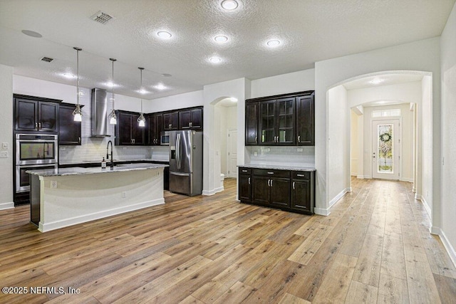 1103 Orchard Oriole Pl, Middleburg, FL 32068 - kitchen featuring appliances with stainless steel finishes, arched walkways, wall chimney range hood, decorative backsplash, and a textured ceiling