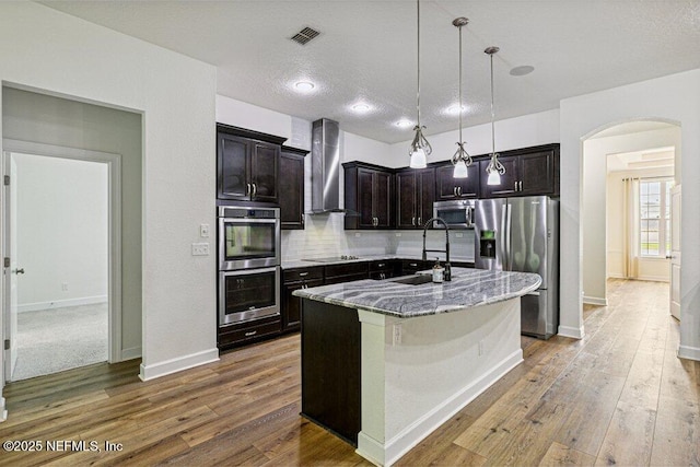 1103 Orchard Oriole Pl, Middleburg, FL 32068 - kitchen with stainless steel appliances, arched walkways, light stone counters, wall chimney exhaust hood, and decorative backsplash