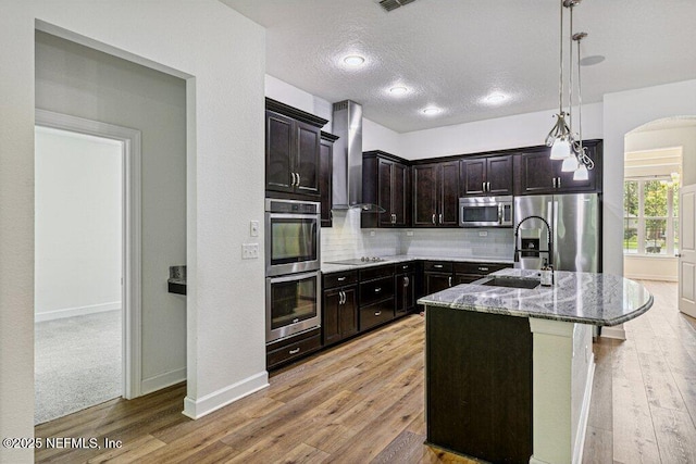 1103 Orchard Oriole Pl, Middleburg, FL 32068 - kitchen featuring stainless steel appliances, wall chimney range hood, dark stone countertops, arched walkways, and tasteful backsplash