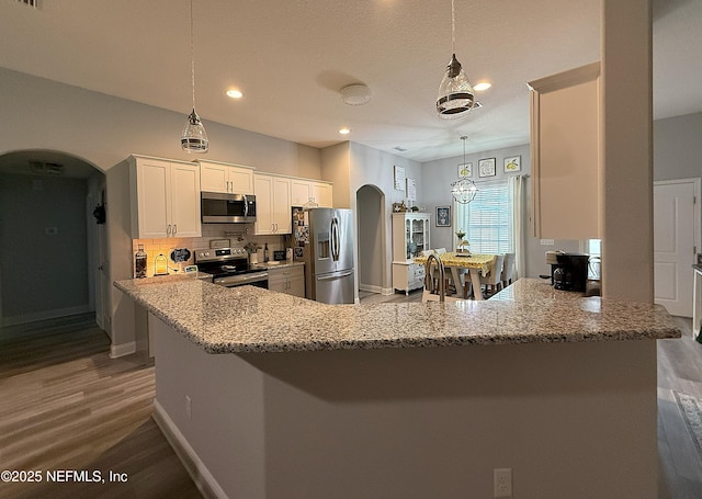 51321 Bloomington Way, Callahan, FL 32011 - kitchen featuring appliances with stainless steel finishes, arched walkways, light wood-type flooring, light stone countertops, and a peninsula