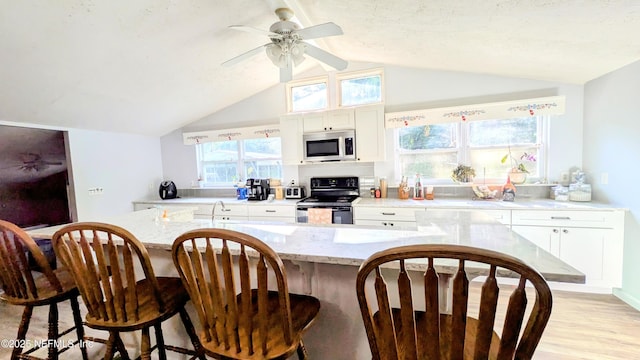 3822 County Road 220, Middleburg, FL 32068 - kitchen with black range with electric stovetop, stainless steel microwave, a breakfast bar, white cabinetry, and ceiling fan