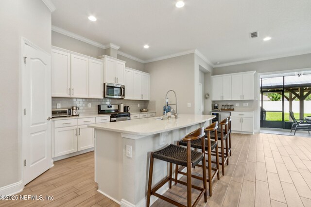 83316 Chapel Ct, Fernandina Beach, FL 32034 - kitchen with stainless steel appliances, light wood finished floors, a kitchen island with sink, tasteful backsplash, and light countertops