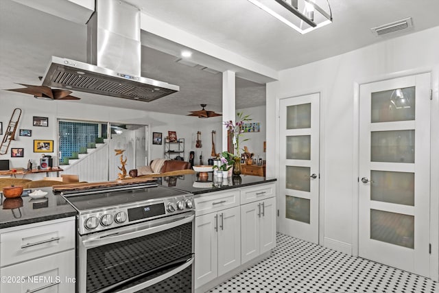 6241 Riviera Manor Dr, Jacksonville, FL 32216 - kitchen with electric range, wall chimney range hood, white cabinetry, dark stone counters, and light flooring