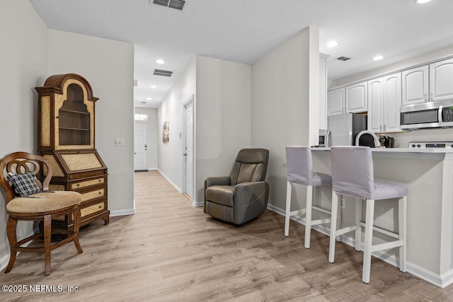 1515 Landau Rd, Jacksonville, FL 32225 - kitchen with stainless steel microwave, freestanding refrigerator, a breakfast bar area, light wood-type flooring, and white cabinets