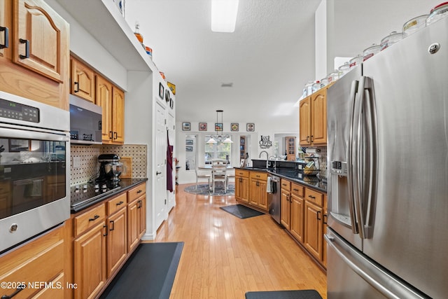 5566 Don Manuel Rd, Elkton, FL 32033 - kitchen with stainless steel appliances, light wood-type flooring, a peninsula, tasteful backsplash, and brown cabinetry