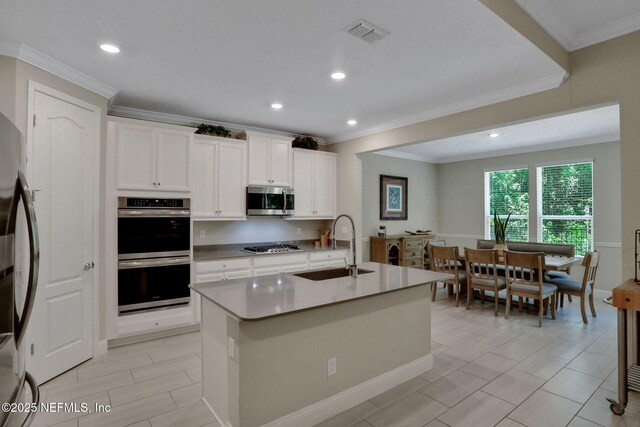 363 Latrobe Ave, Saint Augustine, FL 32095 - kitchen with stainless steel appliances, white cabinetry, an island with sink, light countertops, and ornamental molding