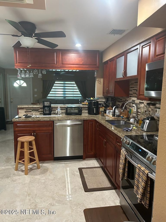 2788 SW 46th Ct, Fort Lauderdale, FL 33312 - kitchen featuring appliances with stainless steel finishes, ceiling fan, tasteful backsplash, a peninsula, and reddish brown cabinets