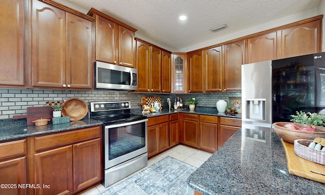 1361 Wekiva Way, Saint Augustine, FL 32092 - kitchen featuring stainless steel appliances, dark stone counters, glass insert cabinets, decorative backsplash, and a textured ceiling
