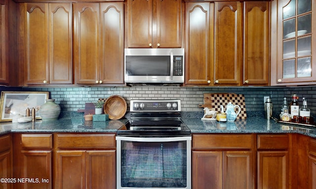 1361 Wekiva Way, Saint Augustine, FL 32092 - kitchen featuring appliances with stainless steel finishes, glass insert cabinets, decorative backsplash, brown cabinets, and dark stone countertops
