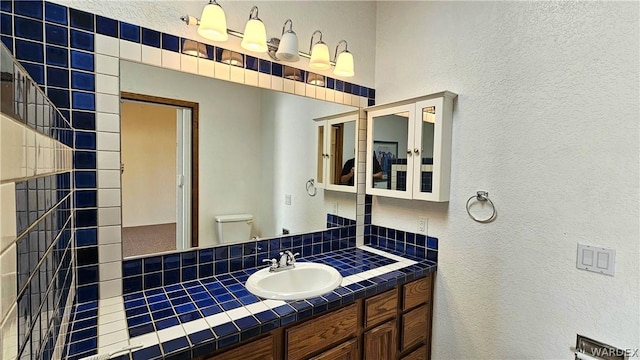 bathroom featuring a textured wall, vanity, toilet, and decorative backsplash