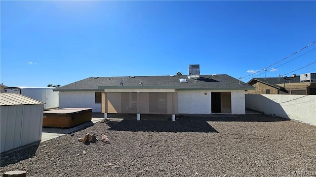 rear view of property featuring a shed, a fenced backyard, and a hot tub