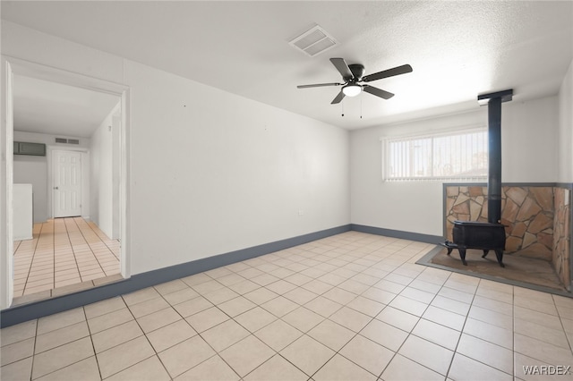 unfurnished living room with light tile patterned floors, visible vents, baseboards, a ceiling fan, and a wood stove