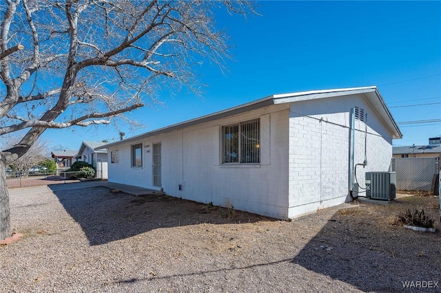 view of side of property with central air condition unit, fence, and brick siding