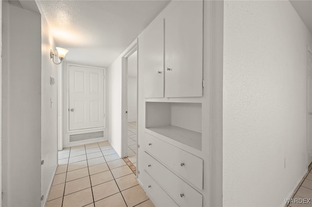 hallway with light tile patterned floors, a textured ceiling, and visible vents