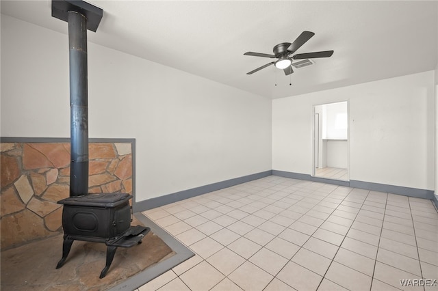 unfurnished living room featuring visible vents, baseboards, ceiling fan, a wood stove, and light tile patterned flooring